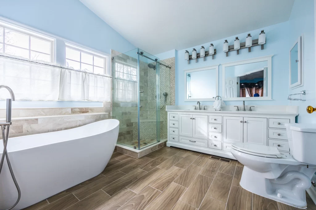 Bathroom remodeling company in Columbia, Howard County, MD, US with double sink vanity, two mirrors, vanity bar lights, corner shower, porcelain tile, freestanding tub, and new toilet.