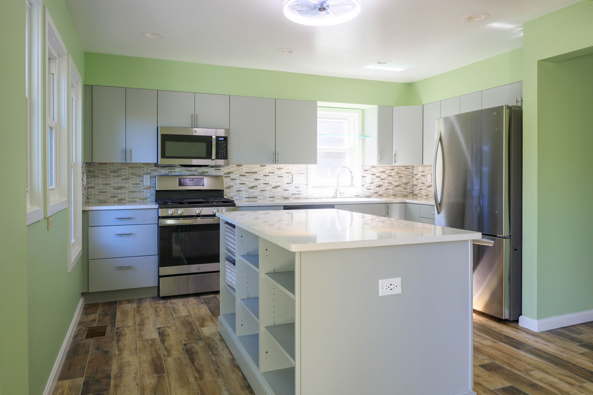 Modern Montgomery County, MD kitchen remodel featuring frameless gray cabinets, quartz countertops, kitchen island with open shelving, backsplash with mosaic glass tiles, wood-look tile floor, recessed lighting, and designer ceiling fan with light.