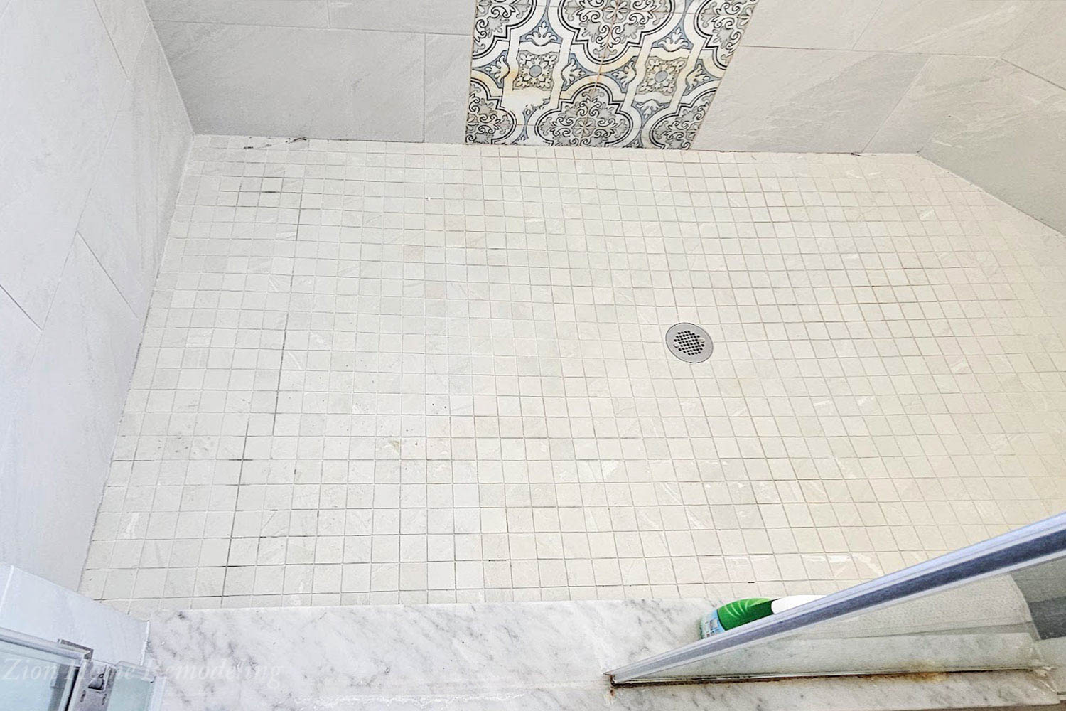 Discolored and stained mosaic shower tiles with failing caulk between tiles and shower floor.