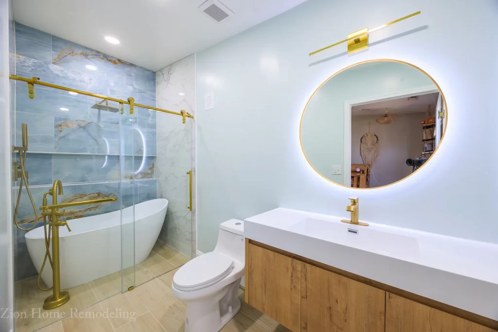 Modern luxury bathroom remodel in Landover, Prince George's County, Maryland, US, with a natural oak floating vanity, round LED mirror with light on, single hole faucet, elegant freestanding bathtub and shower combo, and contemporary tile Zion Home Remodeling, your Maryland expert bathroom remodeler.