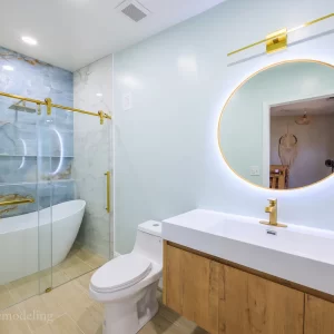 Modern luxury bathroom remodel in Landover, Prince George's County, Maryland, US, with a natural oak floating vanity, round LED mirror with light on, single hole faucet, elegant freestanding bathtub and shower combo, and contemporary tile Zion Home Remodeling, your Maryland expert bathroom remodeler.