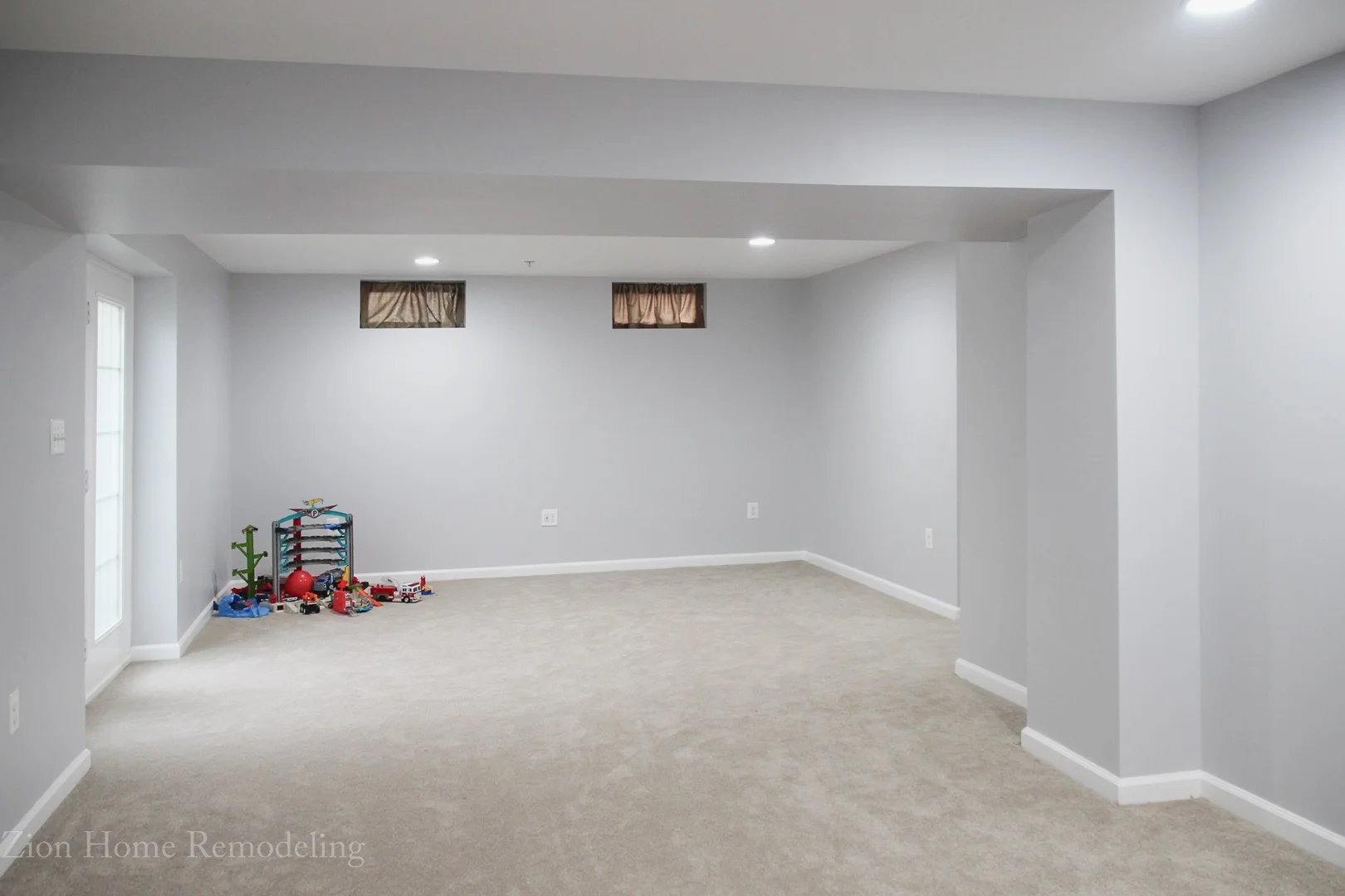 Photo of a complete basement finishing project in Bowie, MD, US with recessed lighting, white ceiling, gray walls, new carpet, and organized kids' toys. Zion Home Remodeling transformed this basement into a functional and beautiful living space, providing basement remodeling services in Bowie, Maryland, USA.